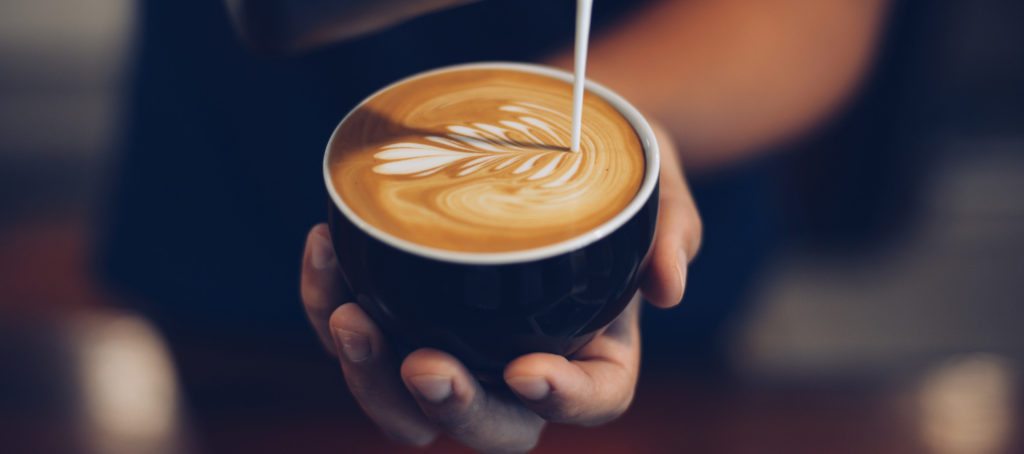 A barista pouring latte art into a latte