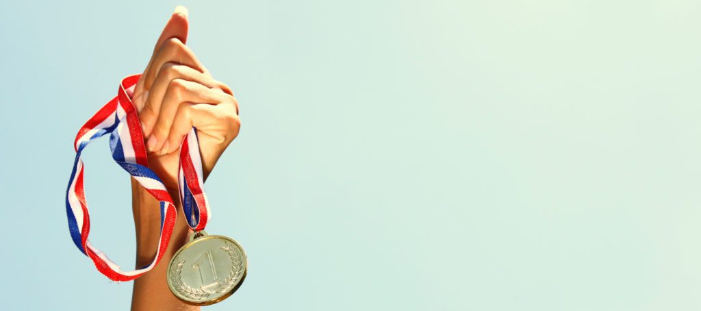 A woman holding a gold medal aloft