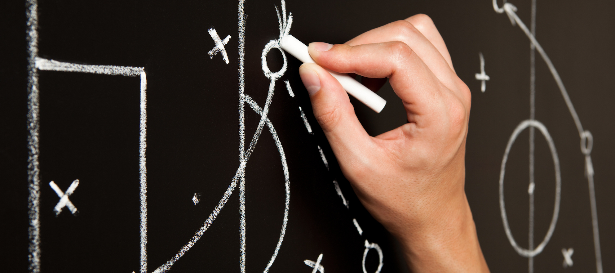 A hand outlining a game plan on a chalkboard