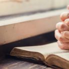 A woman's hands folded on a Bible